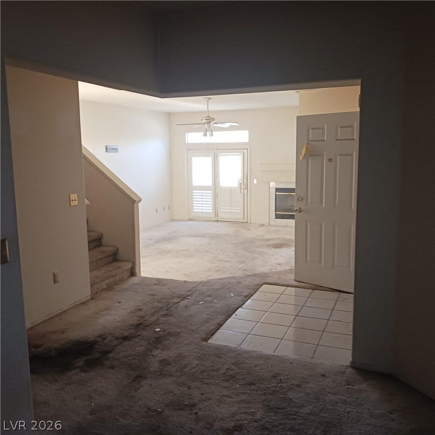 An open entry leads past carpeted stairs into a living space featuring a fireplace.