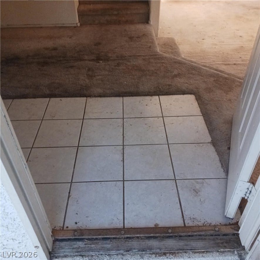 Tiled entryway transitioning into a carpeted living space with split-level stairs.