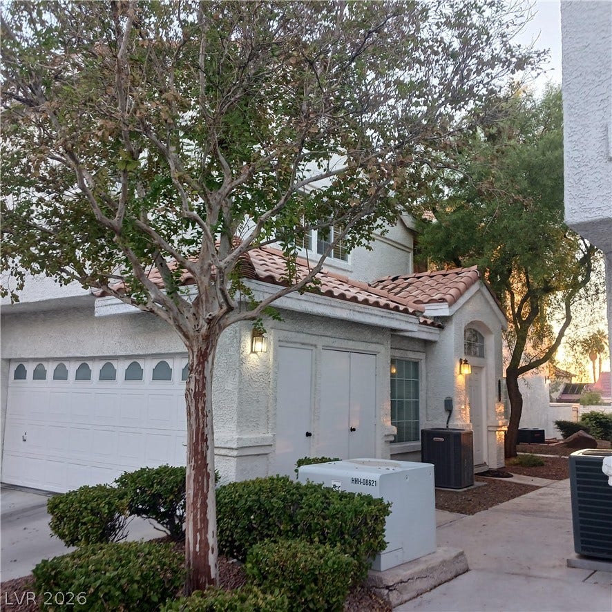 Mature trees shade the stucco exterior of this multi-level residence with tile roofing details.