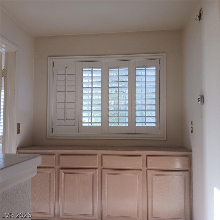 A built-in sideboard sits beneath a large window fitted with plantation shutters.