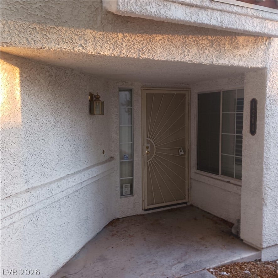 A covered concrete entryway features textured stucco walls and security screen door details.