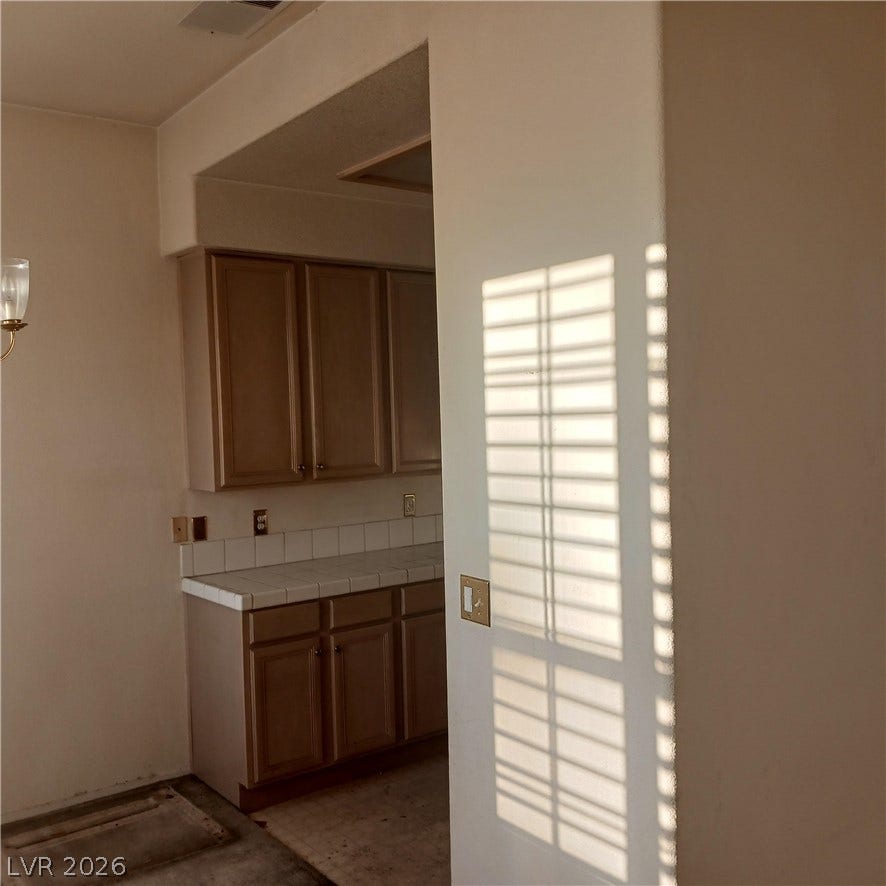 Natural light streams past arched openings into a classic kitchen featuring tile countertops.
