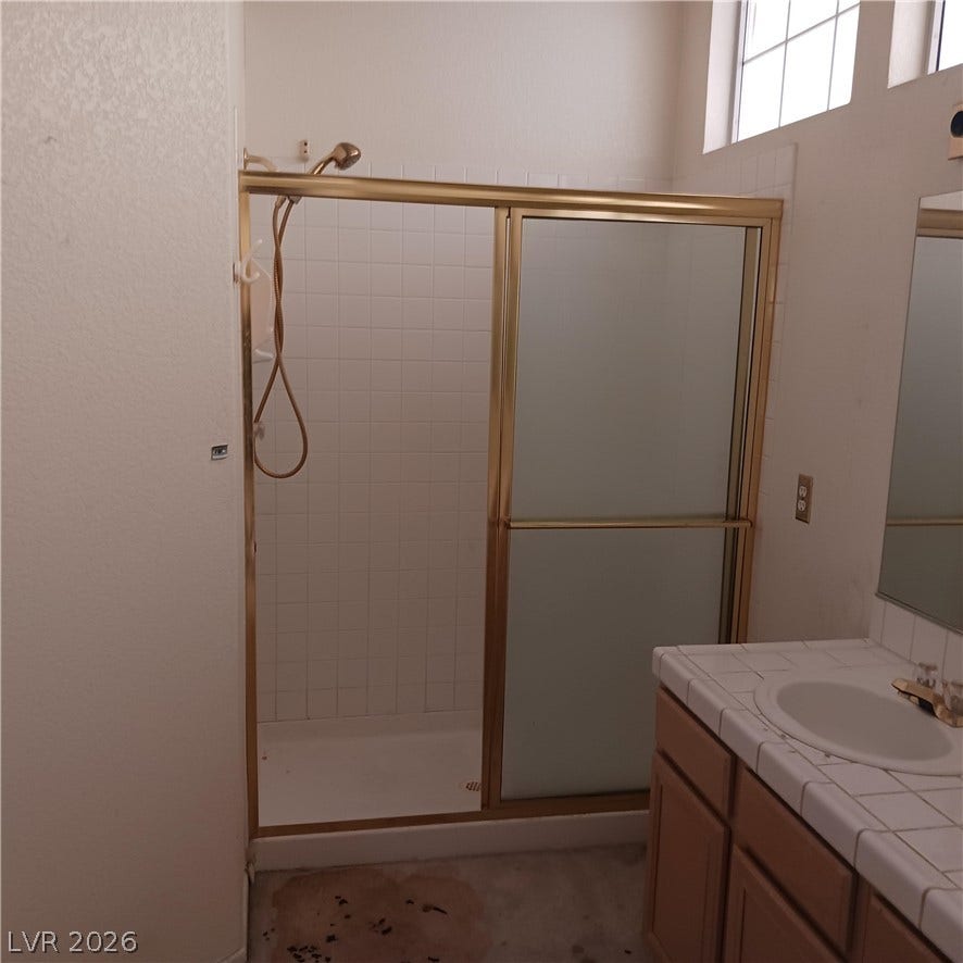 A glass-enclosed shower stall stands adjacent to a tiled vanity in this functional bathroom.
