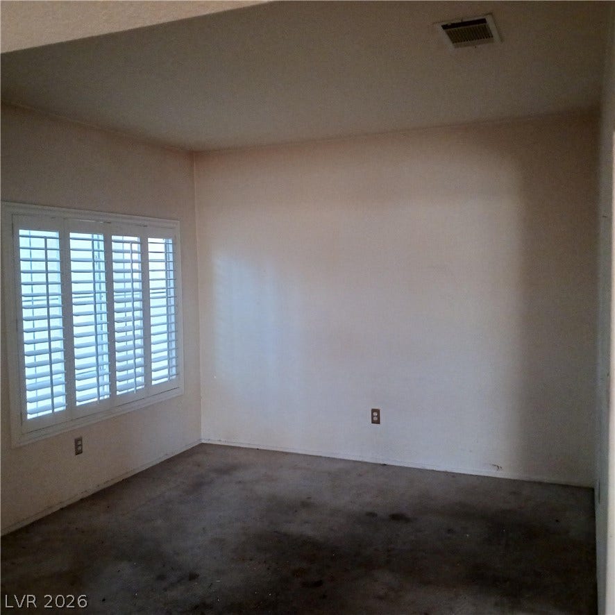 A spacious room features concrete flooring and plantation shutters.