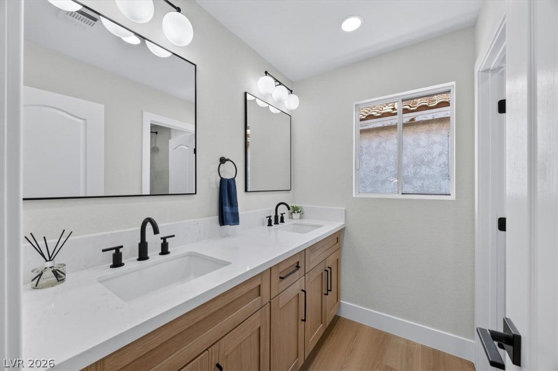 136 Villaggio Street, Henderson, NV 89074 Double vanity featuring clean white counters and warm wood cabinetry below recessed lighting.