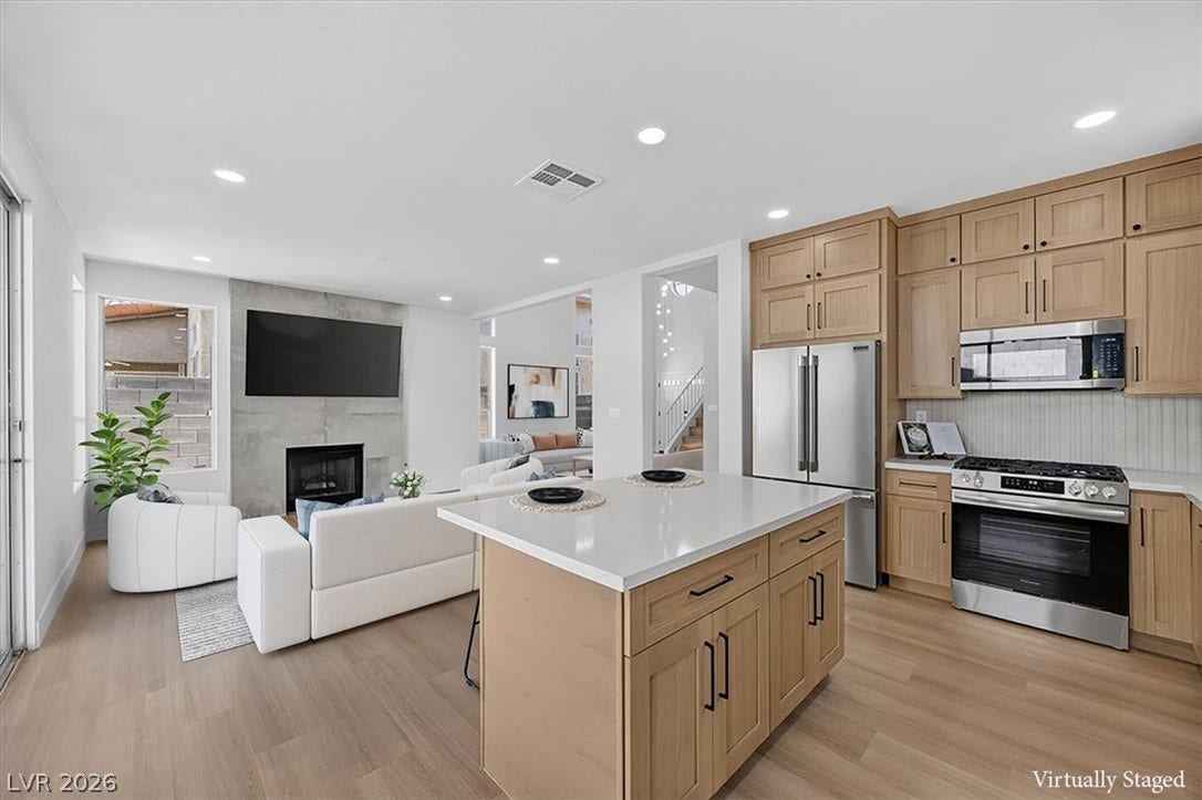 136 Villaggio Street, Henderson, NV 89074 An open layout connects the kitchen to a fireplace-centered living area with wood floors.