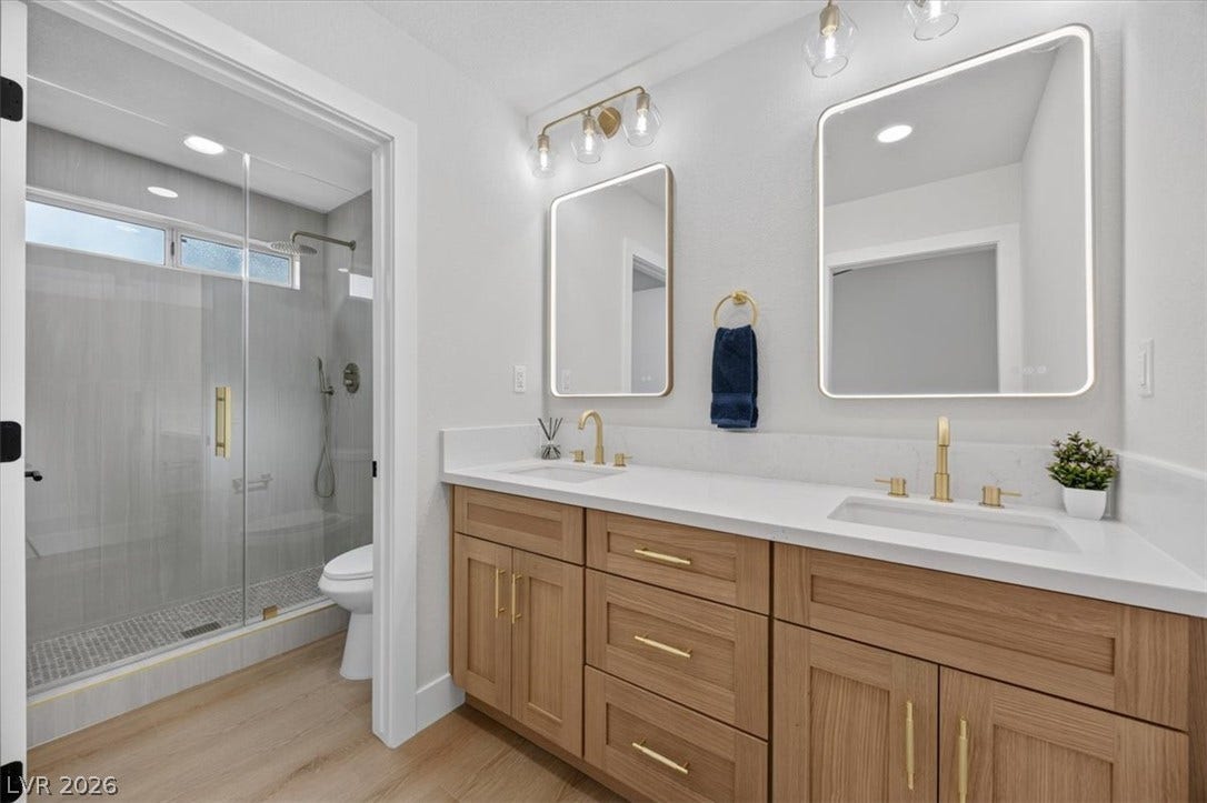 Dual vanity with golden accents offers modern comfort alongside a spacious glass-enclosed shower.