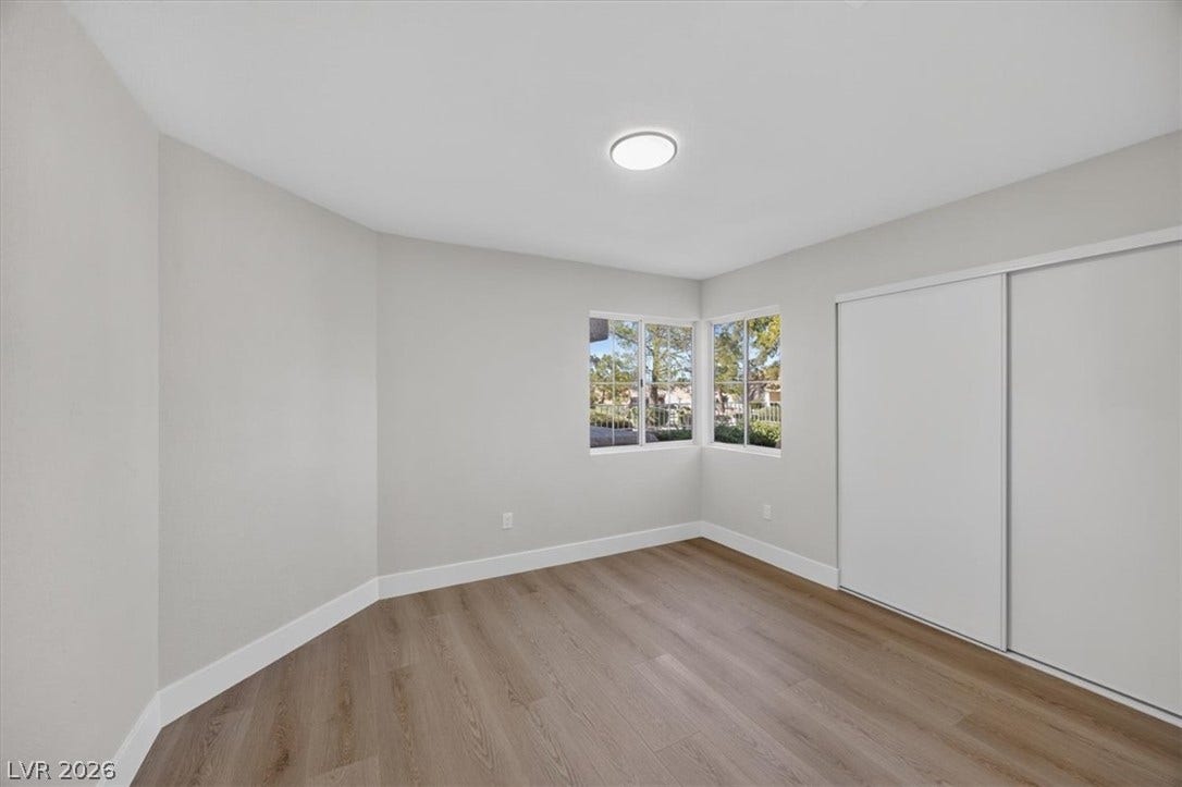 Luminous room features broad windows framing verdant outdoor views and practical sliding closet doors.