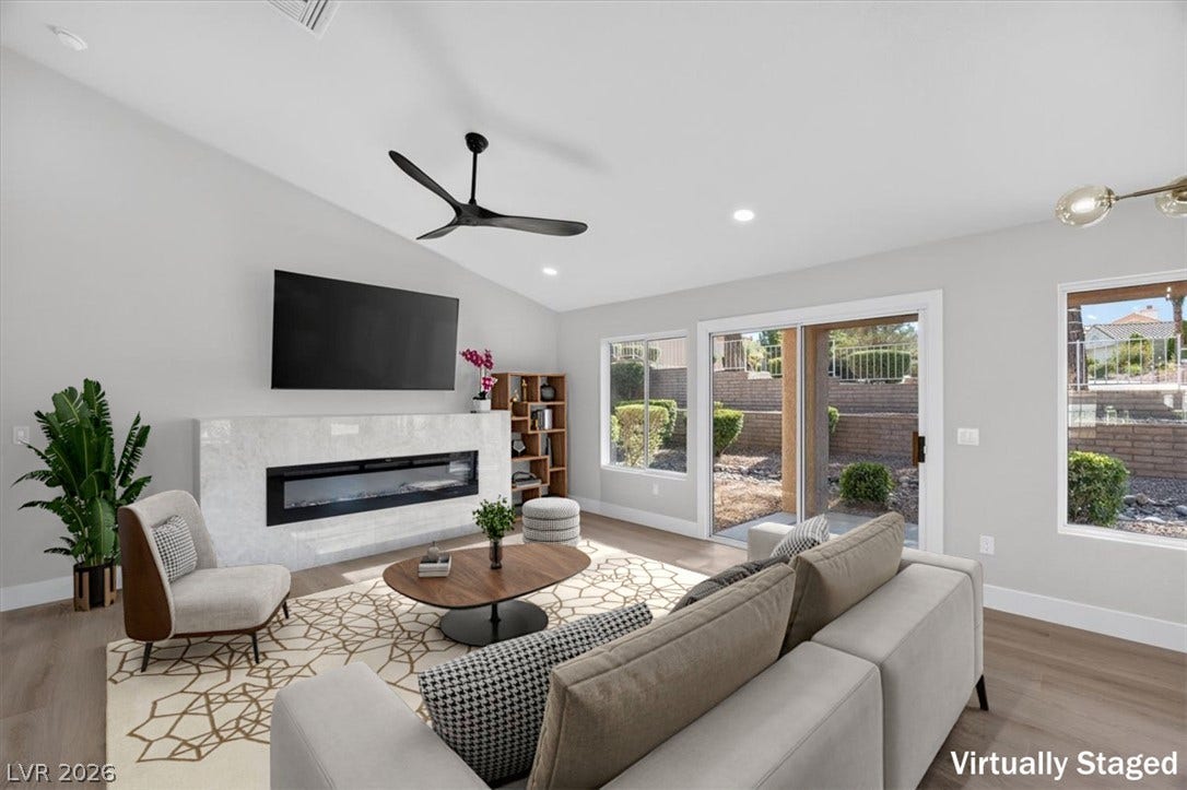 A chic living space featuring a modern fireplace, vaulted ceilings, and views of a landscaped yard.