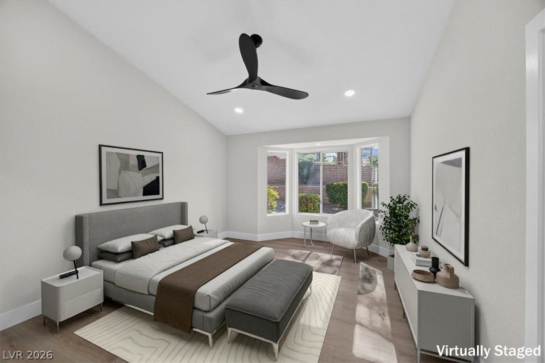 An airy bedroom with vaulted ceilings, featuring a bay window and warm wood flooring.
