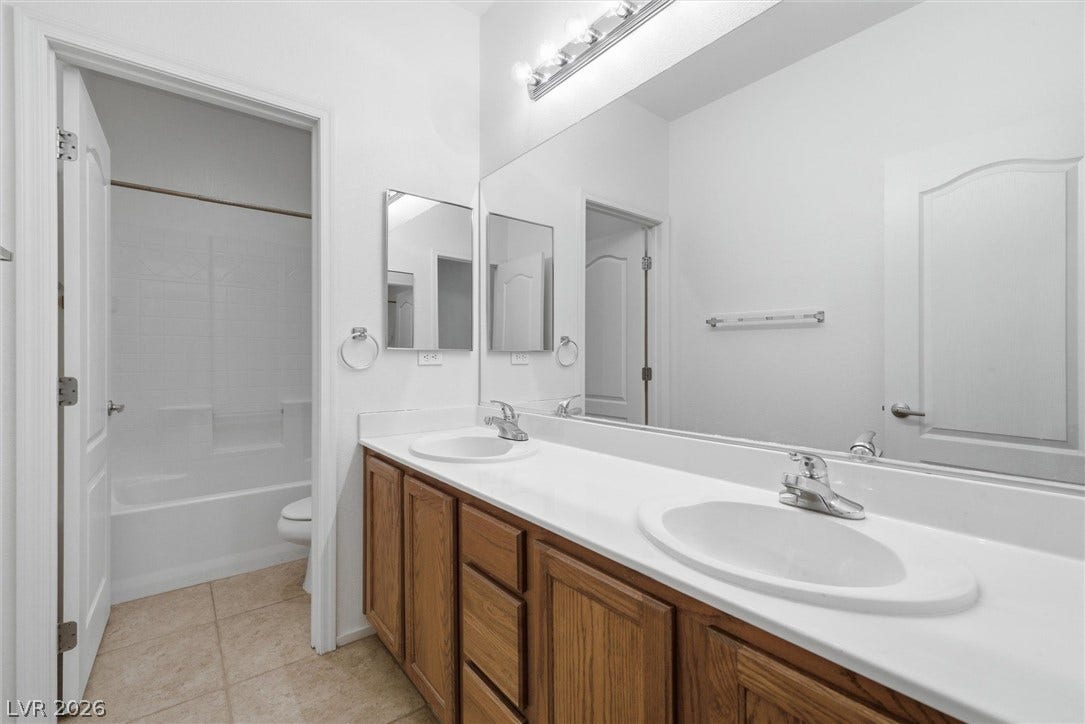4911 S Castello Way, Pahrump, NV 89061 A spacious double vanity features classic wood cabinetry beneath a large wall-to-wall mirror.