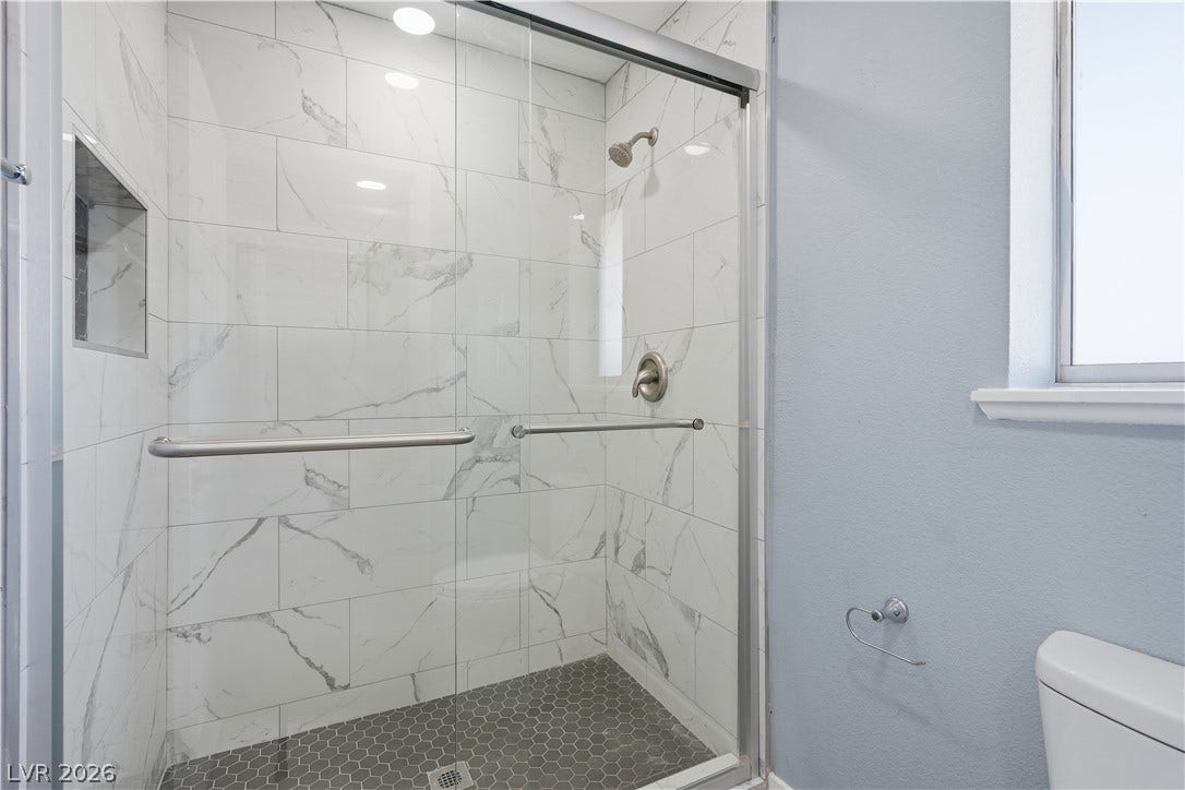 1707 Mapleton Lane, Las Vegas, NV 89119 A modern walk-in shower features marble-look wall tile and a contrasting dark mosaic floor.