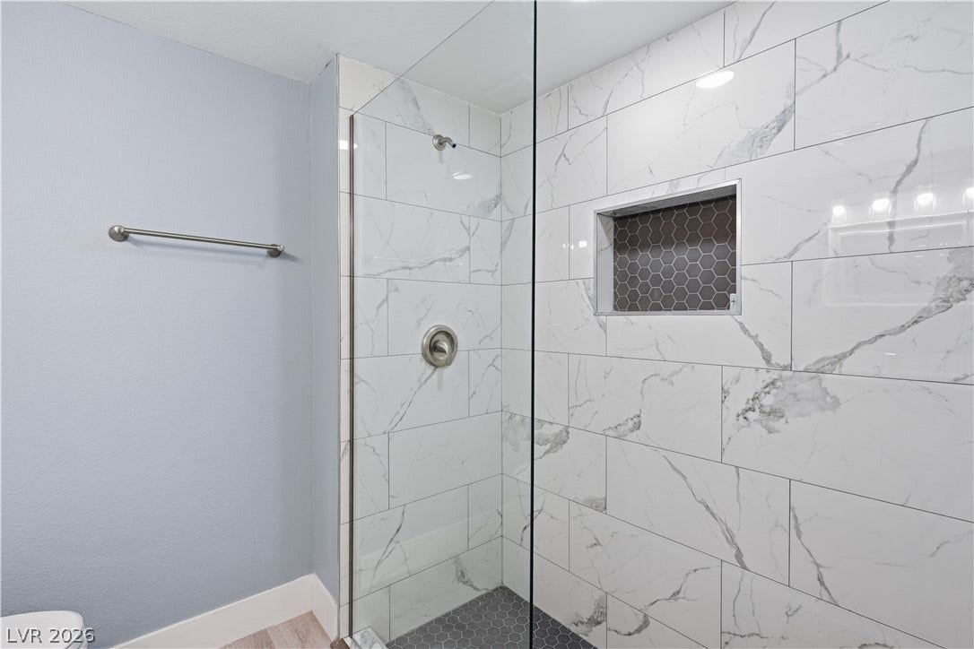 1707 Mapleton Lane, Las Vegas, NV 89119 Floor-to-ceiling marble-patterned tile elevates this modern walk-in shower with a built-in niche.