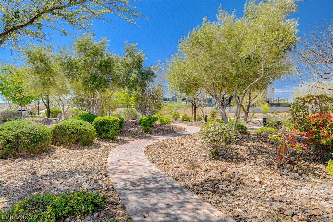 A meandering paved pathway winds through vibrant drought-tolerant landscaping under a brilliant blue sky