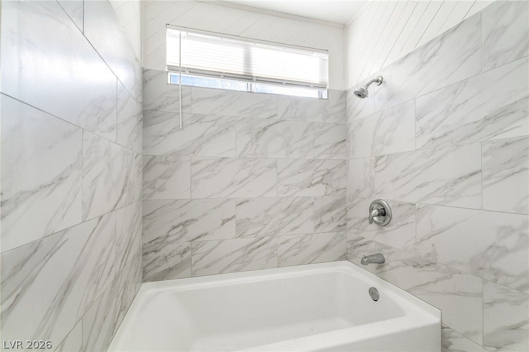768 Panhandle Drive, Henderson, NV 89014 Elegantly veined tile surrounds a deep soaking tub, illuminated by a high window.