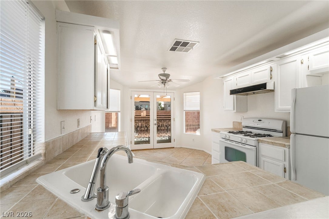 768 Panhandle Drive, Henderson, NV 89014 Tiled countertops and white cabinetry define this functional kitchen layout with French doors leading outside.