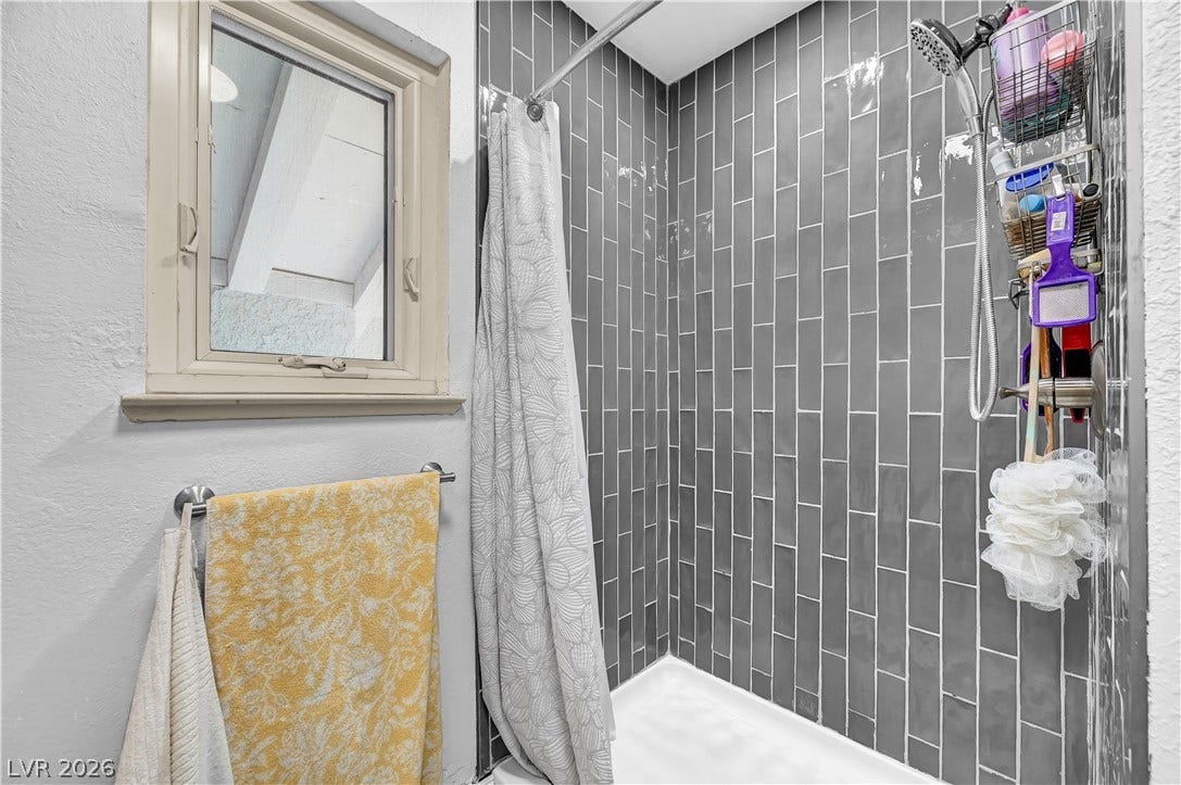 342 Fuente Drive, Henderson, NV 89014 Polished vertical tiling defines a stylish walk-in shower situated beneath a classic wood-framed window.