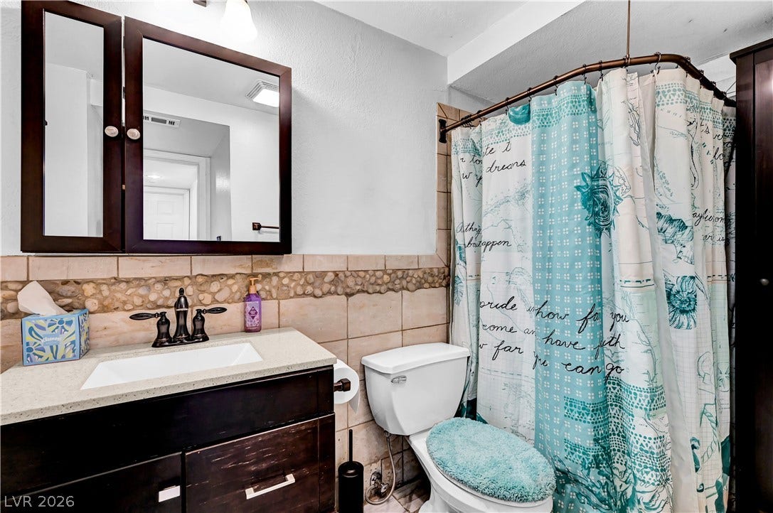 342 Fuente Drive, Henderson, NV 89014 Textured stone detailing frames a dark wood vanity and tiled shower area in this bathroom.