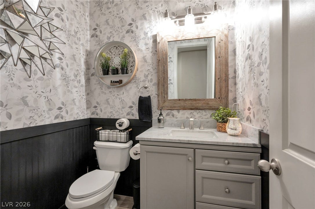 5652 Portage Lake Court, Las Vegas, NV 89130 A powder room features a rustic-framed mirror above a sleek vanity with a marble countertop, complemented by charming botanical wallpaper.