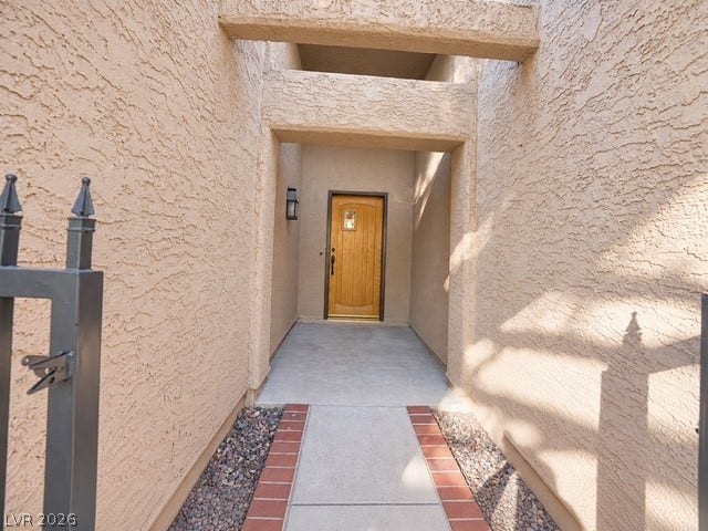 Concrete walkways lead to a recessed entryway framed by structured stucco arches and metal fencing.