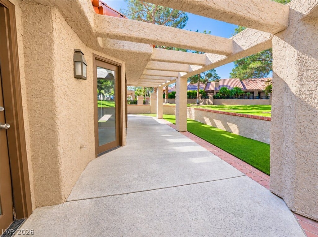 A spacious concrete patio stretches beneath a stucco pergola frame, opening to manicured green space.
