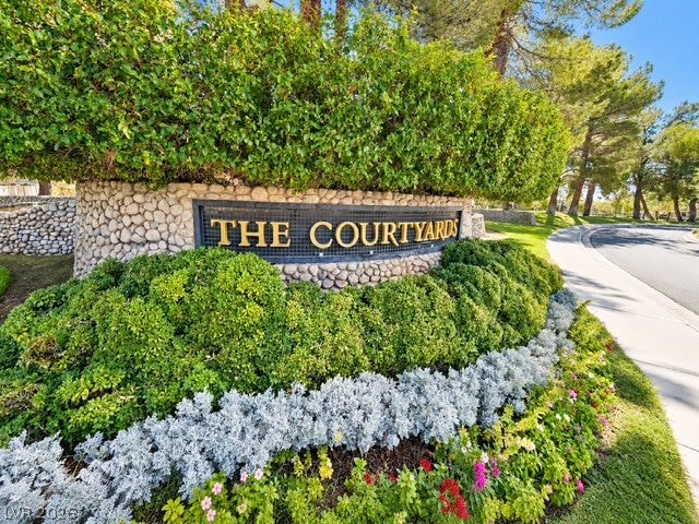 Lush landscaping and stone monumentation frame the community entryway alongside paved sidewalks.