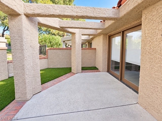 A private concrete patio sits sheltered beneath a textured pergola structure next to sliding glass doors.