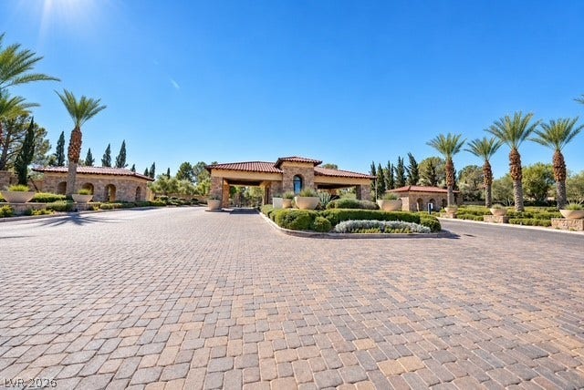 An expansive paver driveway leads toward a secure, beautifully landscaped gated community entrance.