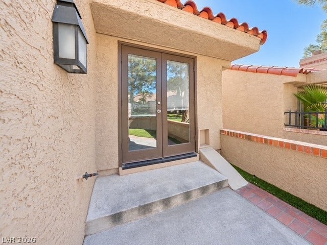 Clay tile roofing and textured stucco walls frame a private entrance with glass French doors.