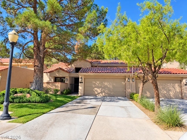 Mature trees frame a concrete driveway leading to a tiled-roof garage.