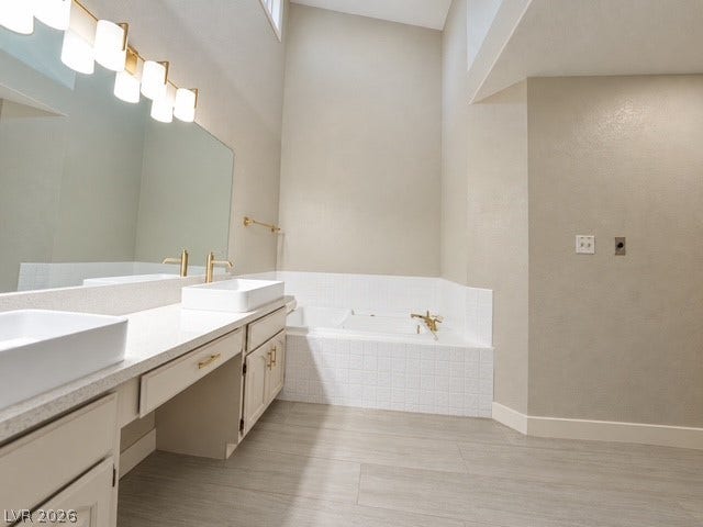 A spacious bathroom features dual sinks and a large soaking tub beneath a high ceiling.