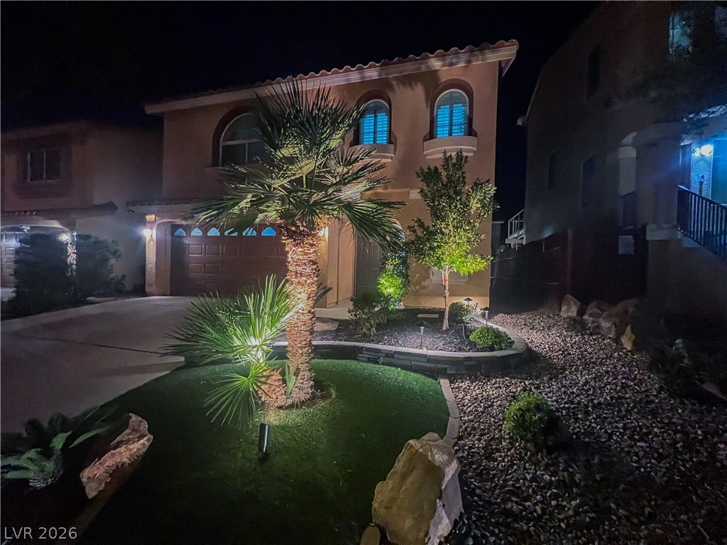 6007 Sonoma Station Avenue, Las Vegas, NV 89139 Dramatic exterior uplighting illuminates the manicured desert landscaping and curved stone garden beds at night.
