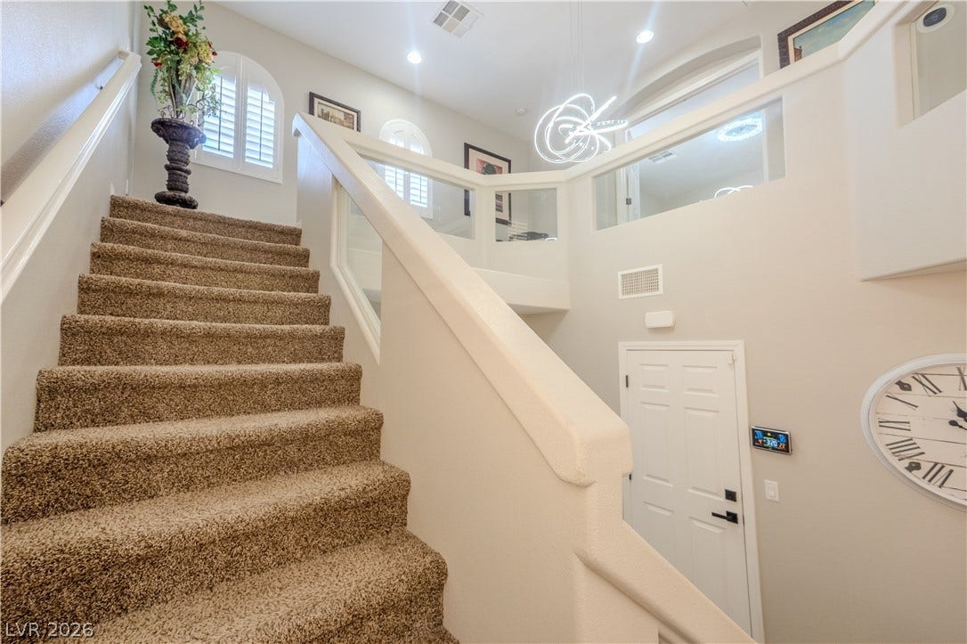 6007 Sonoma Station Avenue, Las Vegas, NV 89139 A carpeted staircase leads past a soaring entryway with contemporary overhead lighting and shuttered windows.