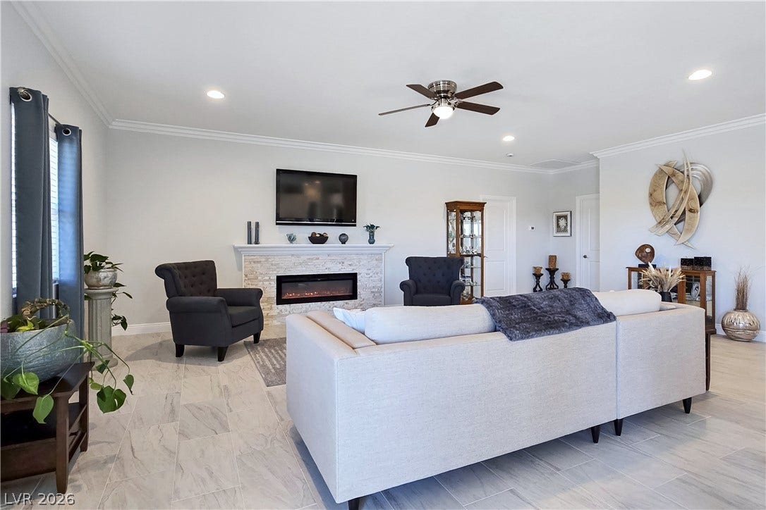 5471 Lincolnwood Court, Pahrump, NV 89061 Crown molding and tiled floors frame a central fireplace in this open living area.
