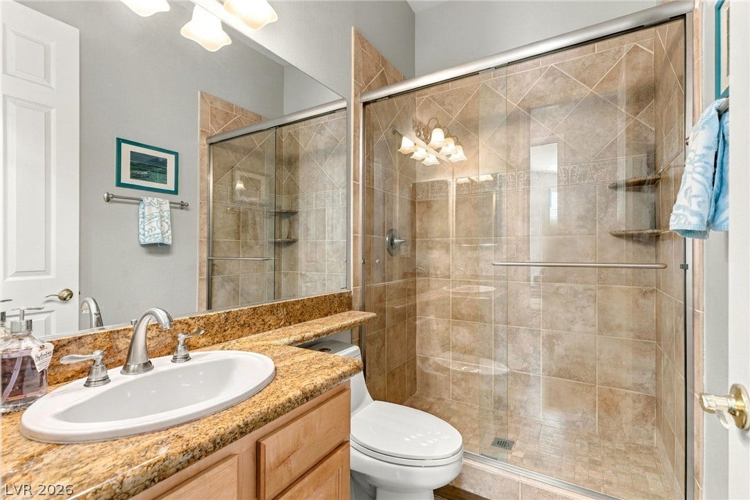2984 Via Della Amore, Henderson, NV 89052 A glass-enclosed walk-in shower with tiled walls stands alongside a granite-topped vanity.