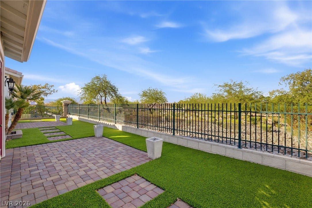 2984 Via Della Amore, Henderson, NV 89052 A paved patio and manicured lawn look out past the secure fencing.