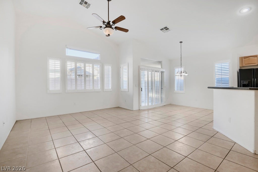 6729 Quarterhorse Lane, Las Vegas, NV 89148 Bright open-concept living space combining the great room, dining area, and kitchen with vaulted ceilings, neutral tile flooring, recessed lighting, ceiling fan, plantation shutters, and abundant natural light. Kitchen features granite countertops, breakfast bar, wood cabinetry, black side-by-side refrigerator, and built-in microwave.