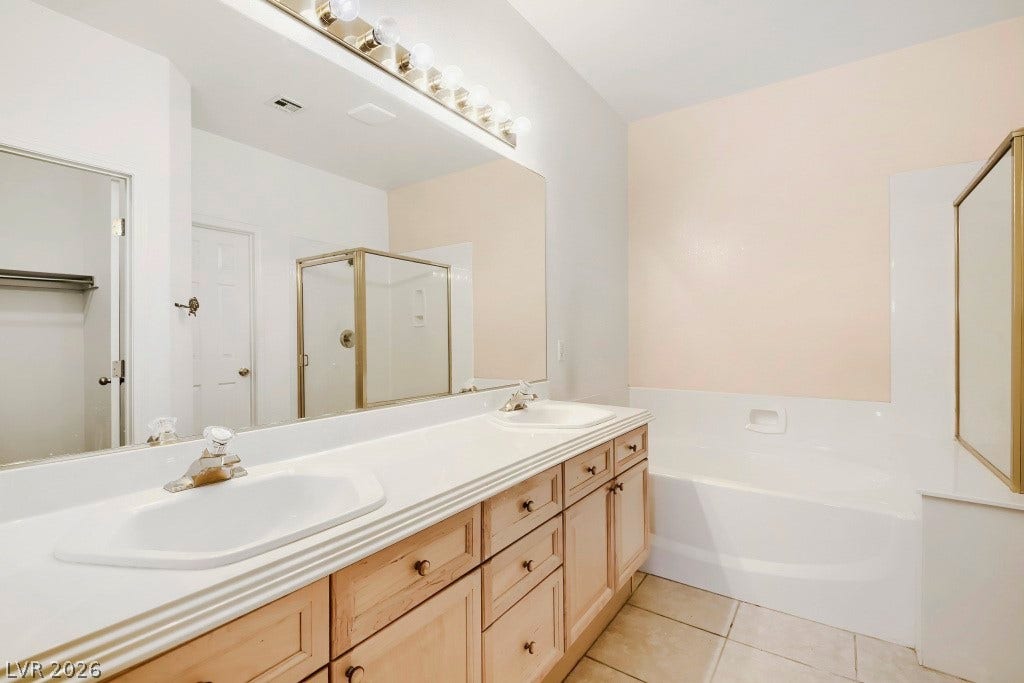 6729 Quarterhorse Lane, Las Vegas, NV 89148 Spacious primary bath featuring a dual-sink vanity with abundant wood cabinetry and drawer storage, oversized wall mirror, vanity lighting, separate soaking tub, glass-enclosed walk-in shower, and neutral tile flooring.