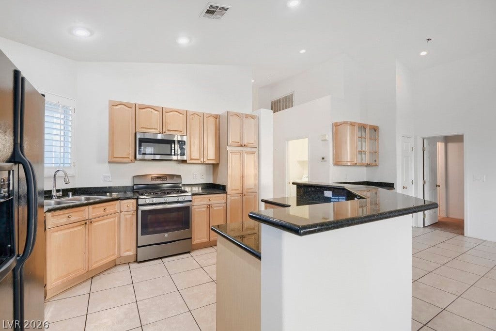 6729 Quarterhorse Lane, Las Vegas, NV 89148 Another view of the kitchen highlighting granite countertops, wraparound breakfast bar, wood cabinetry, stainless steel gas range and built-in microwave, double-basin sink, recessed lighting, and open sightlines into the main living areas.