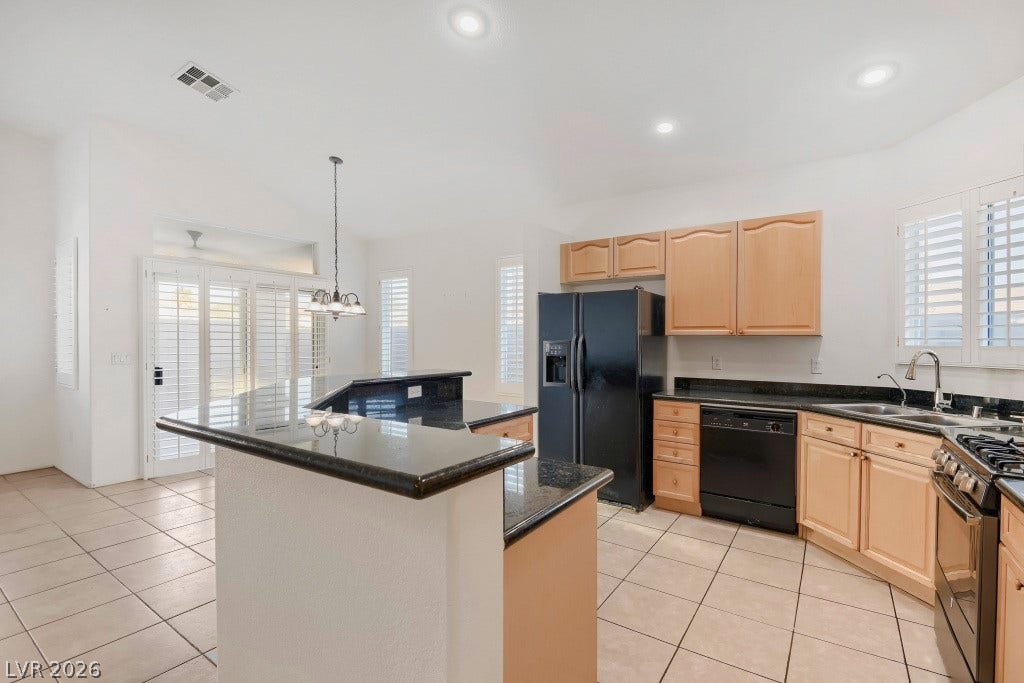 6729 Quarterhorse Lane, Las Vegas, NV 89148 Spacious kitchen featuring granite countertops, wraparound breakfast bar with seating space, wood cabinetry, neutral tile flooring, recessed lighting, double-basin sink, and a full complement of appliances including refrigerator, dishwasher, gas range, and built-in microwave.
