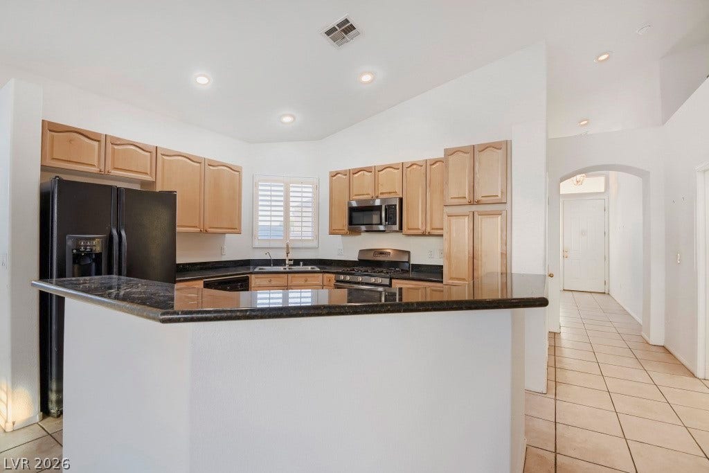 6729 Quarterhorse Lane, Las Vegas, NV 89148 Open kitchen showcasing granite countertops, extended breakfast bar, abundant wood cabinetry, recessed lighting, plantation shutters, and stainless steel gas range with built-in microwave, creating a functional layout with generous counter and storage space.