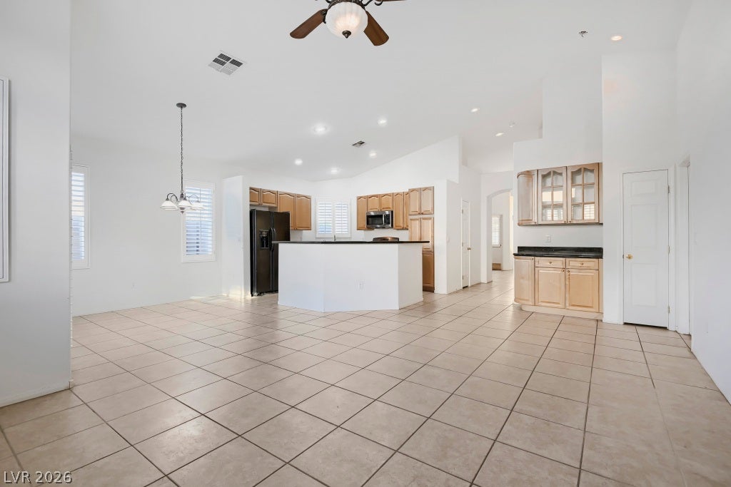 6729 Quarterhorse Lane, Las Vegas, NV 89148 Open-concept great room and kitchen showcasing vaulted ceilings, neutral tile flooring, recessed lighting, breakfast bar with granite countertop, wood cabinetry, and black appliances including a side-by-side refrigerator and built-in microwave.