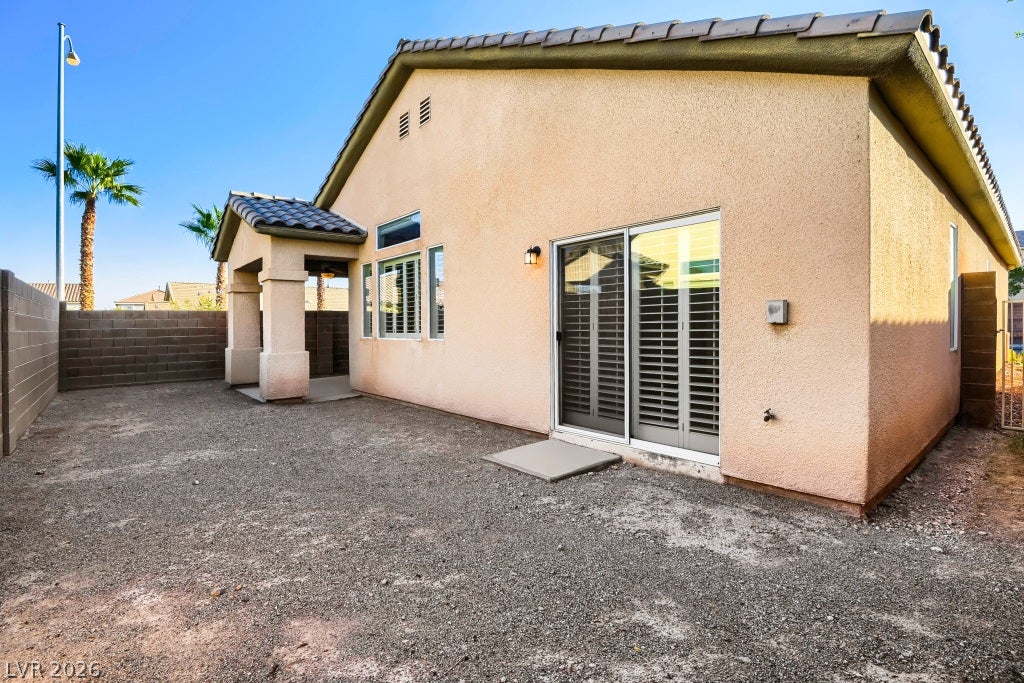 6729 Quarterhorse Lane, Las Vegas, NV 89148 Rear exterior view showcasing the single-story design, tile roof, block-wall enclosed backyard, covered patio, multiple windows with plantation shutters, and additional sliding glass door access to the backyard.