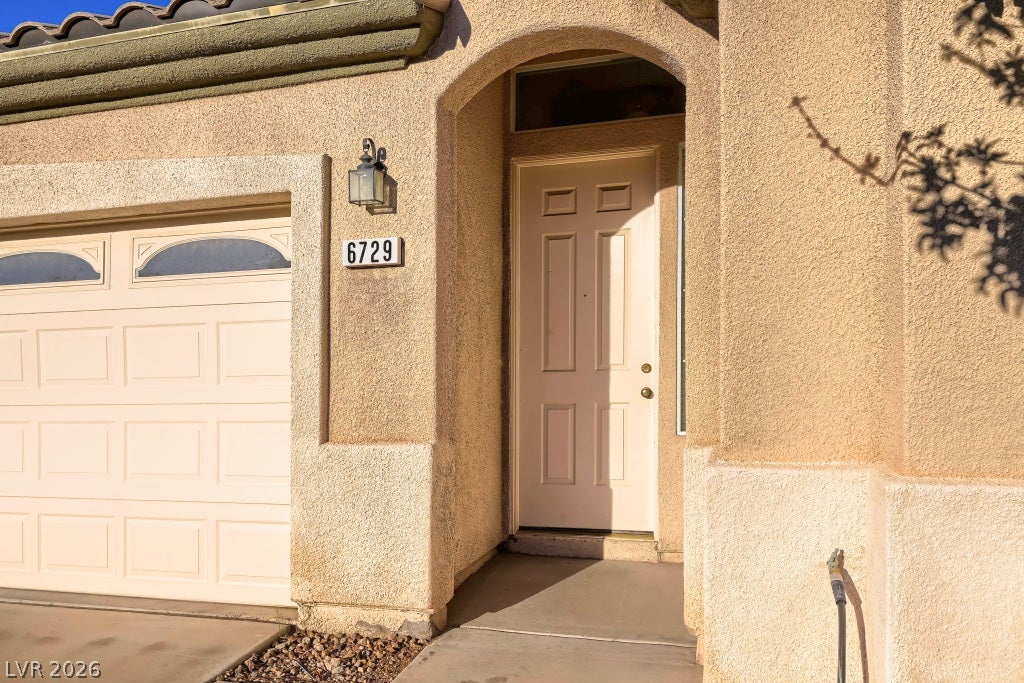 6729 Quarterhorse Lane, Las Vegas, NV 89148 Welcoming covered front entry featuring an arched architectural design, decorative exterior coach lighting, stucco exterior, tile roof, and a recessed entry offering added shade and privacy.