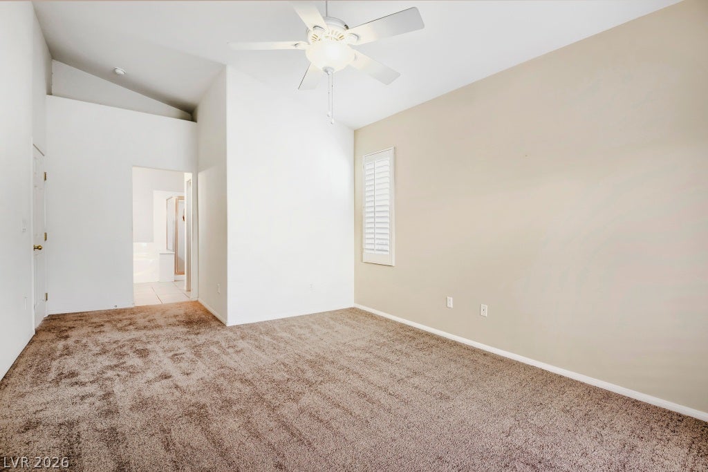6729 Quarterhorse Lane, Las Vegas, NV 89148 Additional view of the primary suite showcasing vaulted ceilings, neutral carpet, ceiling fan, plantation shutters, generous wall space, and direct access to the adjoining primary bathroom.