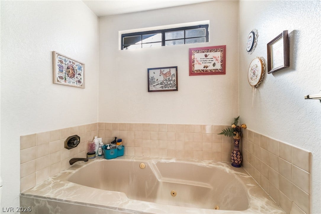 An inviting soaking tub setup features timeless tile accents and a high privacy window.