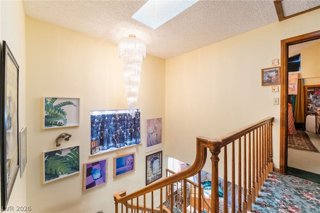 An elegant staircase features wood railings, high ceilings, and a dramatic skylight overhead.