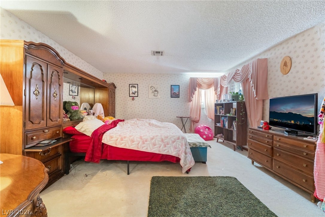 A spacious bedroom offers wall-to-wall carpeting and classic wallpaper detailing.