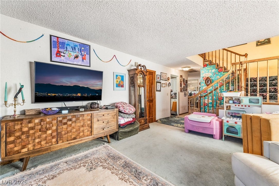 An open living space transitions toward a wooden staircase leading to the upper level.