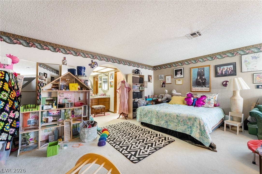 An arched doorway leads from this carpeted bedroom into an adjacent bathroom vanity area.
